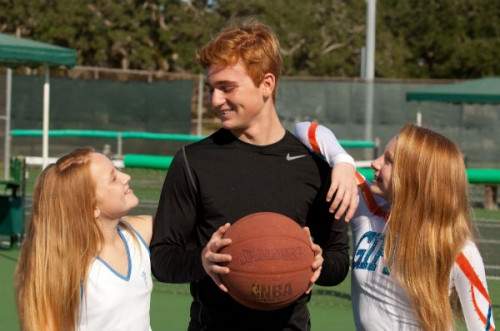 Two girls looking at a boy playing basketball